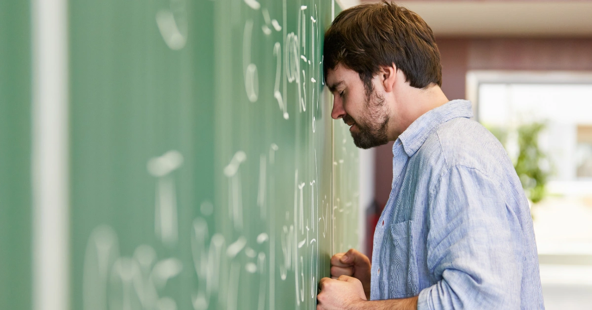 A man standing with his head against a chalkboard