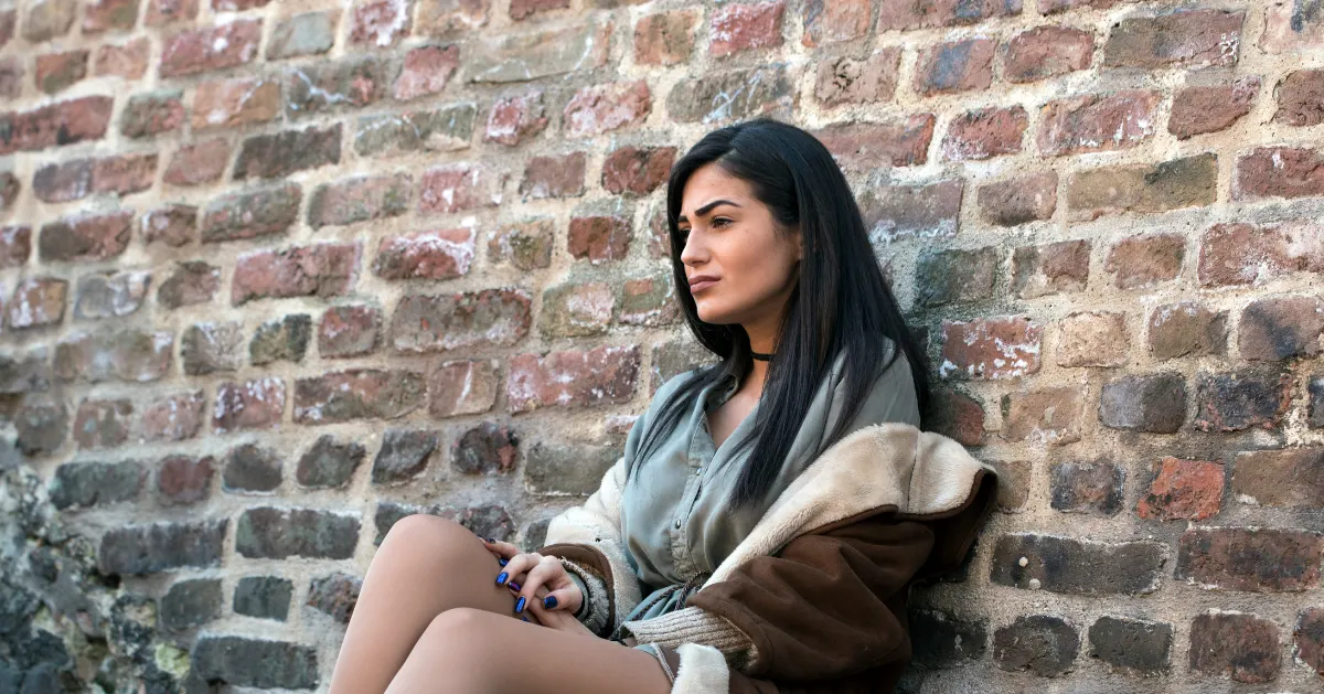 a girl sitting with her back on a brick wall