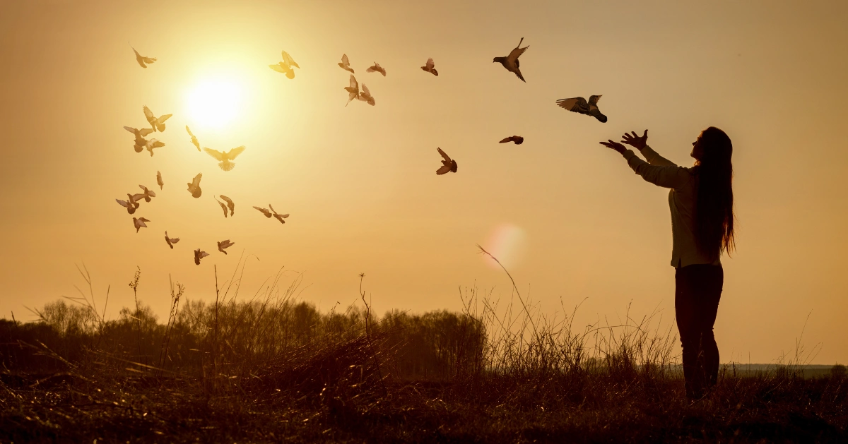 a girl with her hands out as birds fly by giving the illusion she released the birds
