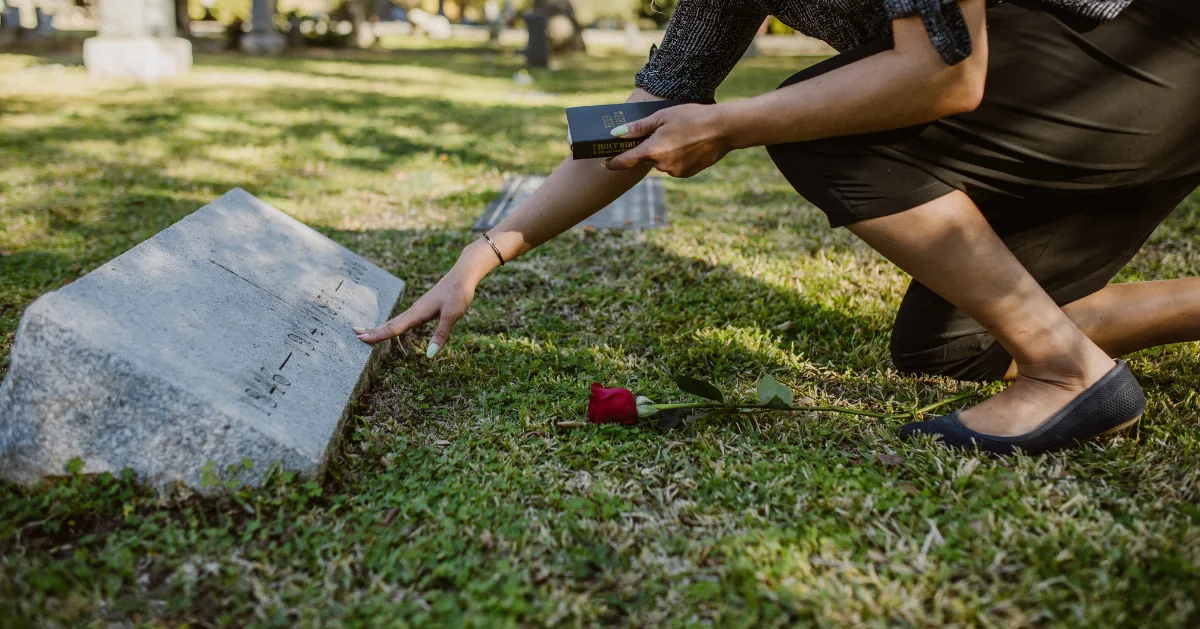 someone placing a rose at near a tombstone